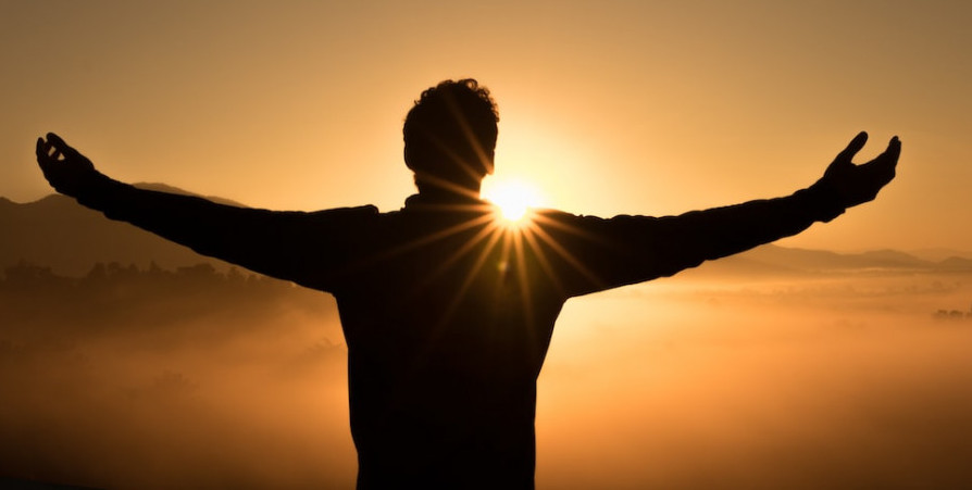 Picture of a man with arms stretched out facing the sunset