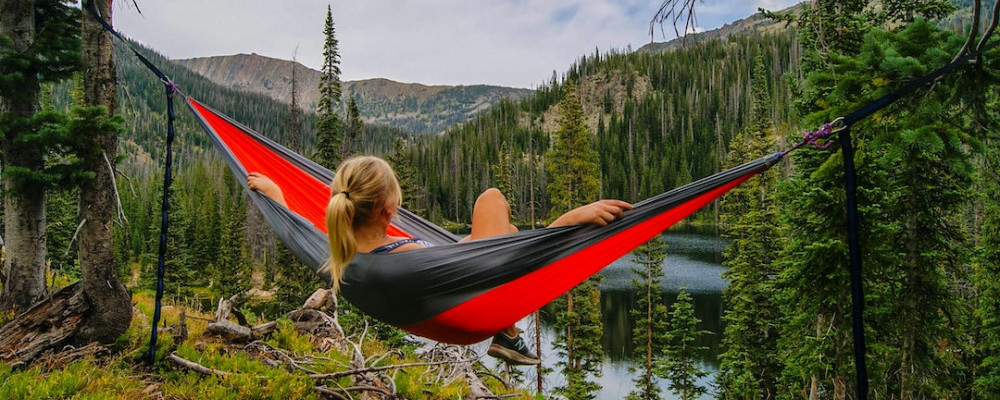 A woman is resting inside a hammock, looking out at nature.