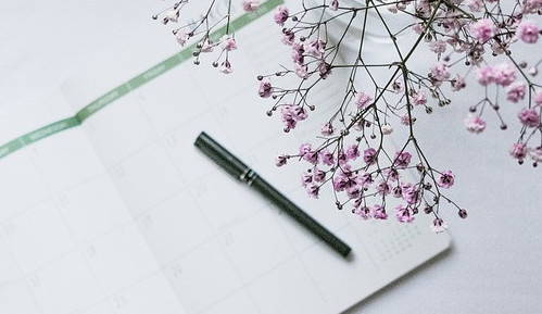 Picture of an open calendar planner with a black pen laying across it and small lavender flowers next to it.