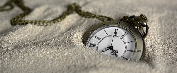 A pocket watch laying on top of sand with a portion of it covered.