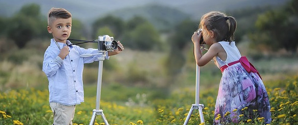 Two small children taking pictures of each other in a field of small yellow flowers.